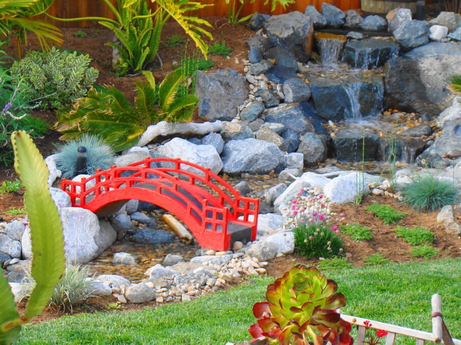 A beautifully designed red bridge installed over a water feature in a rock garden
