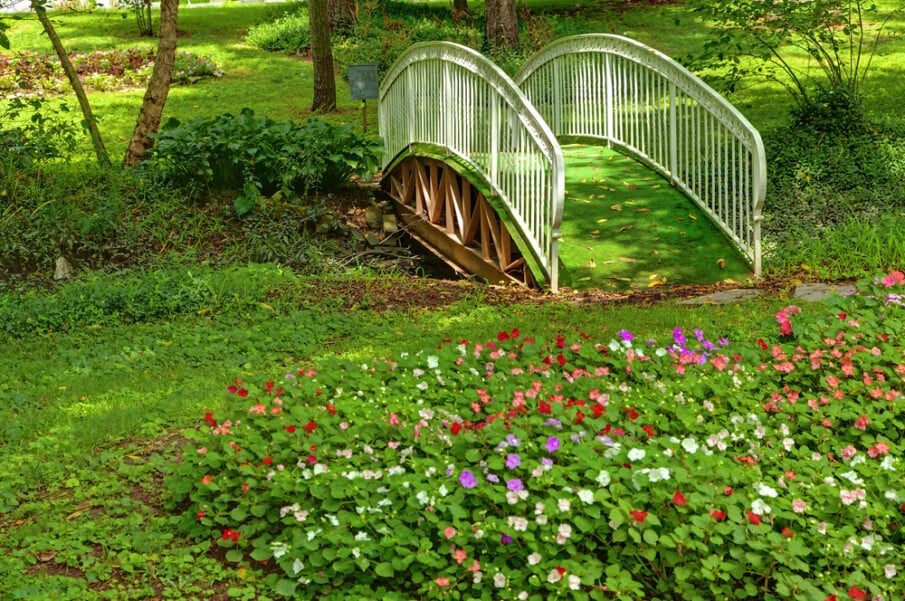 A garden bridge with metal white railings is covered with artificial grass
