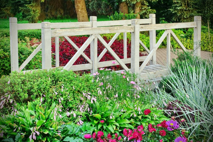 A wood bridge featuring crossbuck railings connects brick patio with a garden