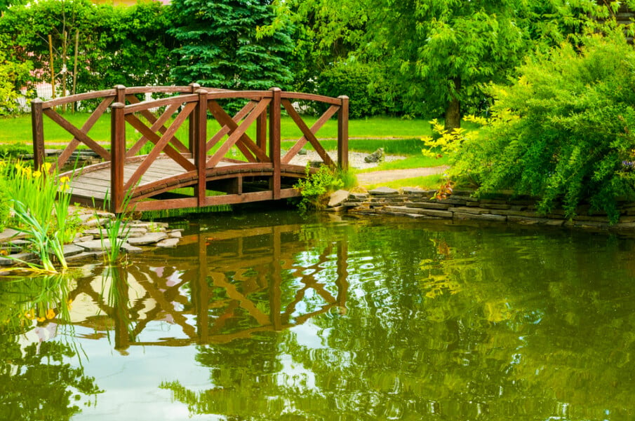 A pond bridge with an arched design that inclides crossbuck railings