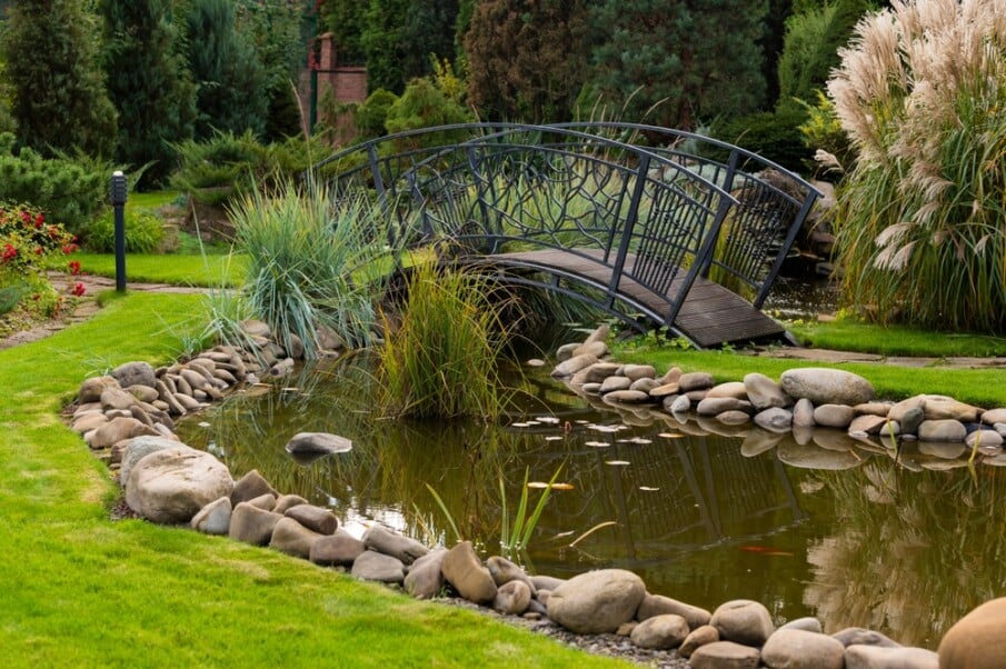 An arched wrought iron bridge placed over a garden pond