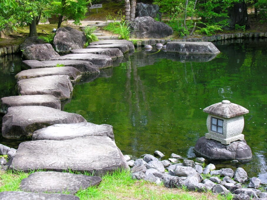 Stepping stones laid in a shallow pond, with Japanese lattern placed on one shore